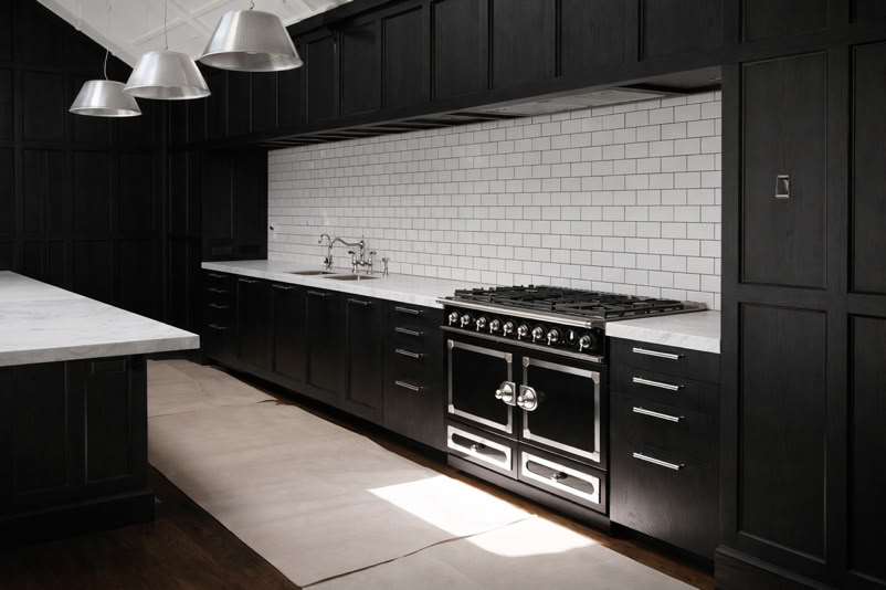 A modern kitchen with dark cabinets, a white subway tile backsplash, a large black oven, and three metallic pendant lights hanging above a white countertop.