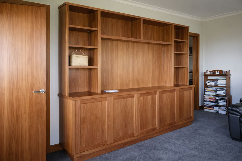 Wooden bookshelf with multiple shelves and cabinets, a closed door on the left, and a small shelf with items on the right.