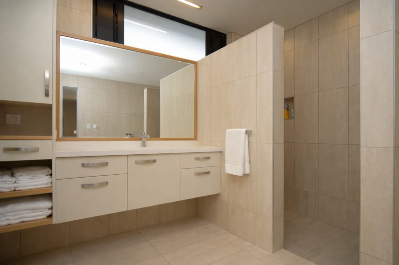 Modern bathroom with a large mirror above a sink, beige cabinets, and a walk-in shower with a towel hanging on the wall.