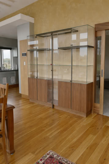 Wooden display cabinet with glass doors in a room with wooden flooring and a small portion of a rug visible.